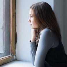 A girl sitting deep in thought, looking out of a window.