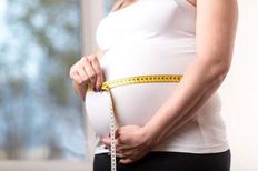Беременная женщина измеряет сантиметровой лентой обхват живота.