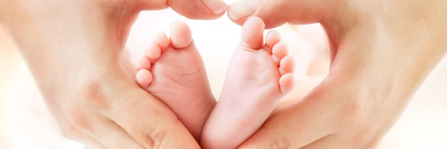 Die Hände einer Frau formen ein Herz um die Füße eines Kindes.
