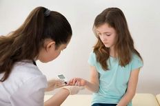 Kadın bir doktor bir kız çocuğunun kan şekerini parmağından ölçüyor.