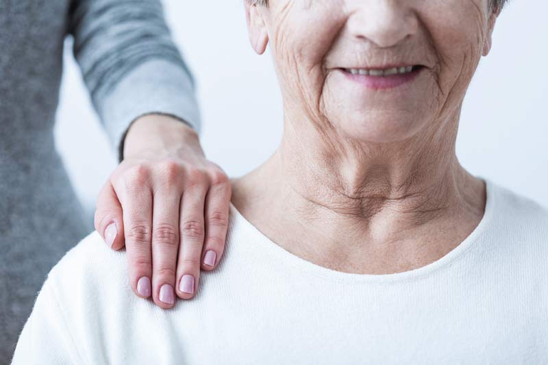 Eine junge Frau legt die Hand von hinten auf die Schulter einer älteren Frau