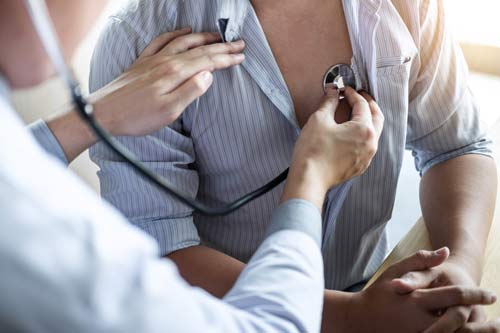 Eine Ärztin hört mit einem Stethoskop das Herz eines Patienten ab.
