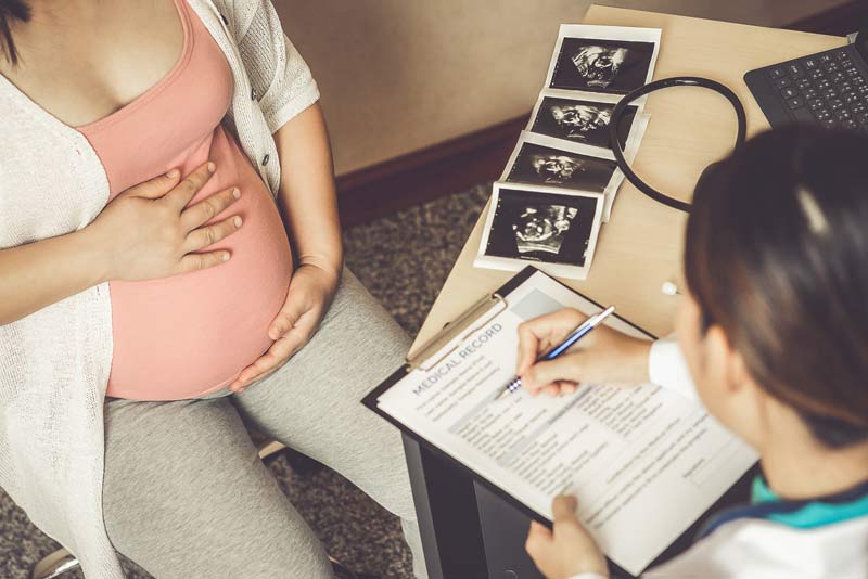 Eine schwangere frau im Gespräch mit einer Ärztin, die einen Anamnese-Fragebogen ausfüllt.