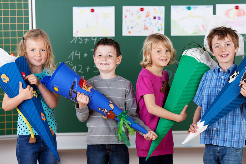 4 Kinder stehen mit ihren Schultüten vor einer Tafel