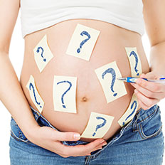 Schwangere Frau hat Notizzettel mit Fragezeichen auf dem Bauch.