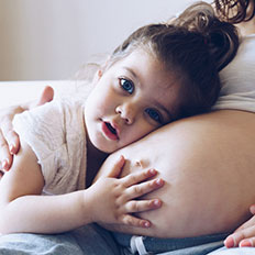 Kleinkind umarmt Bauch der schwangeren Mutter.