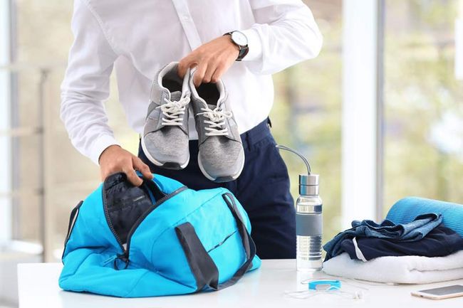 Ein Mann in Hemd und Anzugshose packt seine Sporttasche. 