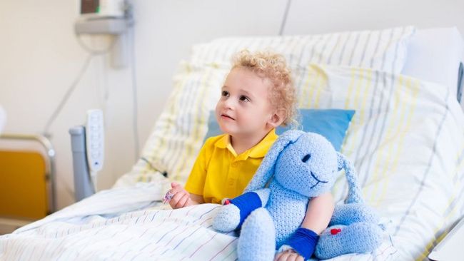 Ein Kleinkind sitzt mit einem kuscheltier in einem Krankenhausbett