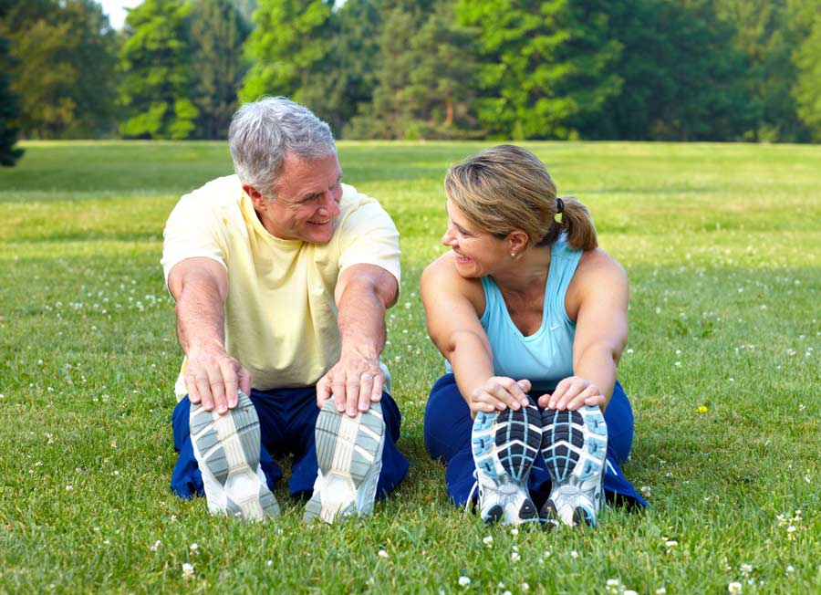 Ein Mann und eine Frau sitzen in Sportkleidung in einem Park und dehnen sich.