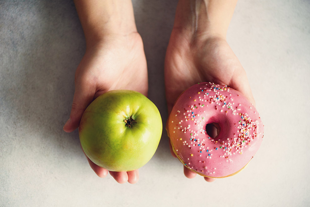 In einer Hand liegt ein Apfel, in der anderen Hand ein Donut.